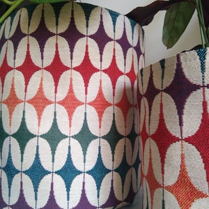 Peut inclure: Deux pots de plantes en tissu avec un motif géométrique de cercles et de diamants rouges, orange, verts, turquoise et violets. Les pots sont en tissu tissé.