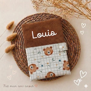 Peut inclure: Une pochette rectangulaire composée d'une partie supérieure en velours côtelé marron avec le prénom Louis brodé en blanc et d'une partie inférieure à motif quadrillé blanc, têtes d'ours et petites fleurs, fermée par un bouton-pression.
