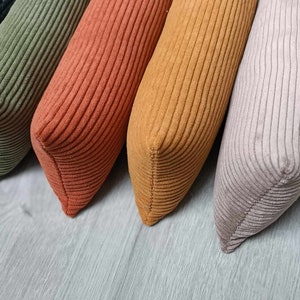 Peut inclure: Une collection de six coussins en velours côtelé de différentes couleurs : noir, vert olive, orange brûlé, jaune moutarde, mauve et crème. Les coussins sont disposés en diagonale, mettant en valeur leur tissu texturé et leur forme rectangulaire. Il s'agit d'un article de décoration.