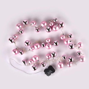 May include: A string of pink, iridescent, round ornaments with built-in LED lights. The lights are strung on a clear wire and are powered by a battery pack.