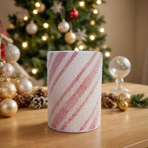 May include: A white cylinder candle with pink and white candy cane stripes. The candle is covered in white glitter.