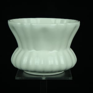 Może przedstawiać: Biały ceramiczny wazon z żebrowanym wzorem. Wazon ma szeroki otwór i zaokrągloną podstawę.
