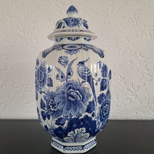 Pode incluir: Um pote de gengibre de cerâmica branca e azul com tampa, apresentando um design floral e de pássaros detalhado. O pote tem formato bulboso e é decorado com intrincados padrões azuis. A tampa é encimada por um pequeno botão.