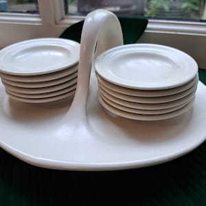 May include: A white ceramic serving tray with a handle and two stacks of white ceramic saucers.