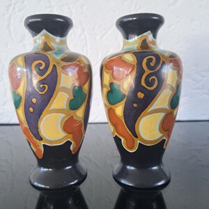 May include: Pair of small, black ceramic vases with colorful, abstract designs. The vases have a yellow, orange, green, blue, and gold pattern.