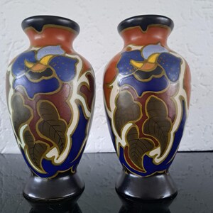 May include: A pair of ceramic vases with a floral design. The vases are decorated with blue, red, green, and yellow flowers and leaves. The vases are about 6 inches tall.