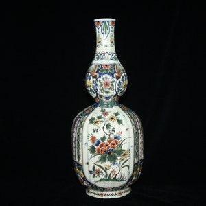 May include: A white ceramic vase with a bulbous body and a long neck. The vase is decorated with a colourful floral pattern in shades of blue, green, red, and yellow.