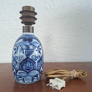 May include: A table lamp base featuring a blue and white ceramic body with intricate floral and geometric patterns. The lamp has a dark metal socket at the top and includes a beige electrical cord with a two-prong plug attached to the base.