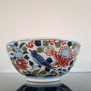 May include: A white ceramic bowl with a blue, red and green floral pattern. The bowl has a round shape and a wide rim.