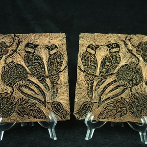 May include: Two wooden printing blocks featuring intricate designs of birds and leaves. The blocks are made from light brown wood and have a dark brown stain. They are both mounted on small wooden stands.