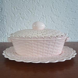 Gran sopera ovalada antigua de Waechtersbach, de color rosa, con asas de mimbre y pomo en forma de huevo en la tapa.