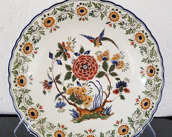 Könnte beinhalten: Ein weißer Keramikteller mit einem blauen, grünen, gelben und roten Blumendesign. Der Teller zeigt einen Vogel im Flug und einen gewellten Rand.