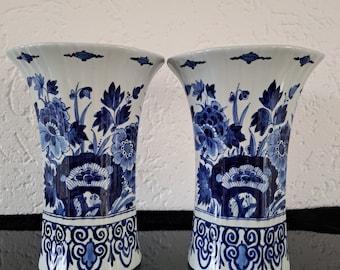 May include: Two white ceramic vases with blue and white floral designs. The vases have a flared top and a round base. The floral designs are intricate and detailed.