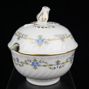 May include: White porcelain sugar bowl with a lid and a gold trim. The bowl has a floral design with blue flowers and gold leaves.