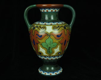 May include: A green and white ceramic vase with two handles and a floral design. The vase has a brown rim and a green base.