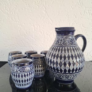 Może przedstawiać: Zestaw sześciu niebieskich i białych ceramicznych kubków z wzorem diamentowym i pasującą dzbankiem. Kubki i dzbanek mają wypukły, biały wzór.