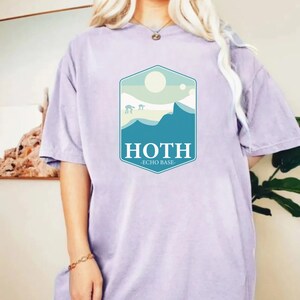 May include: A lavender t-shirt with a graphic of a mountain range and the text "HOTH - ECHO BASE" in a blue and white hexagonal design.