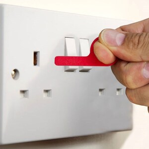 Puede incluir: Una toma de corriente blanca con tres interruptores y una cubierta de seguridad de plástico rojo. La cubierta se utiliza para bloquear el acceso a la toma de corriente.