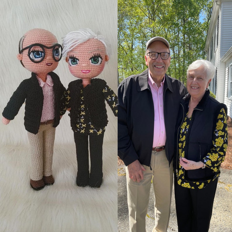May include: A crocheted couple doll set, the woman is wearing a black jacket with gold stars and the man is wearing a black jacket with a pink shirt. The dolls are standing on a white surface.