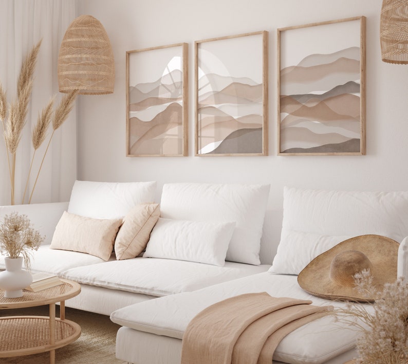 May include: A white sectional sofa with a light brown throw blanket and a straw hat on the chaise lounge. The sofa is in front of a white wall with three framed abstract art prints featuring brown and beige colors.