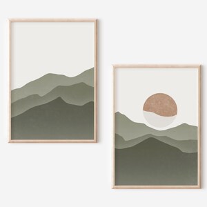 Op de afbeelding: Twee ingelijste prints met abstracte landschapsontwerpen. De eerste print toont een groene bergketen met een witte achtergrond. De tweede print toont een groene bergketen met een witte achtergrond en een bruine cirkel in het bovenste midden.