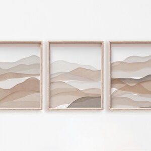 May include: Three framed prints with abstract watercolor-style landscapes in shades of brown and beige. The prints are arranged in a row, with the frames aligned.