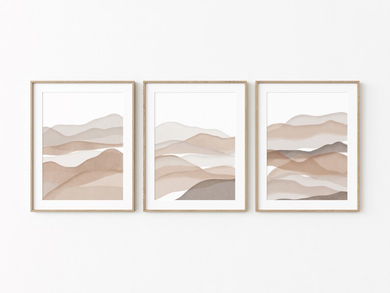 May include: Set of three framed abstract art prints featuring watercolor-style landscapes in shades of brown, beige, and gray. The prints are in simple wooden frames.