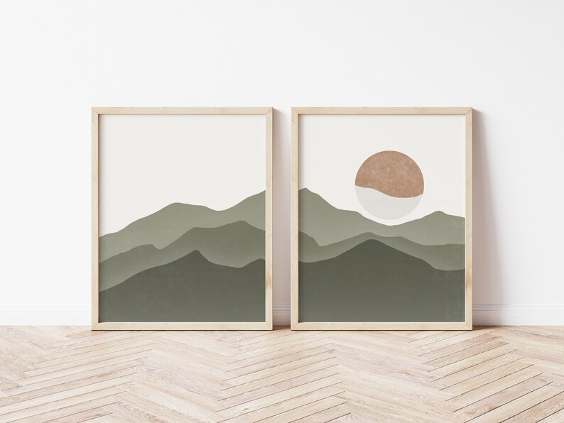 Op de afbeelding: Twee ingelijste prints met abstracte berg- en zonontwerpen. De linker print toont een groene bergketen met een witte achtergrond. De rechter print toont een groene bergketen met een witte achtergrond en een bruine zon met een wit centrum.