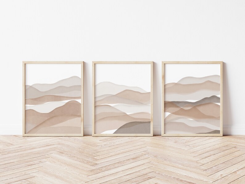 May include: Three framed prints with abstract watercolor-style landscapes in shades of brown and beige. The prints are arranged in a row on a light wood floor.