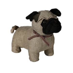 May include: A fabric pug dog doorstop in tan with black features. The pug has a black snout and ears, and a brown ribbon. The doorstop is designed to stand upright and has a small tail. A decorative item for the home.