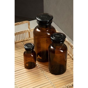 May include: Three amber glass bottles with black lids on a woven bamboo tray. The bottles are of different sizes and are arranged in a row.