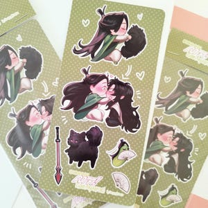 Puede incluir: Hojas de pegatinas con ilustraciones de estilo anime de dos personajes besándose, abrazando a una criatura negra y esponjosa, y otras imágenes relacionadas. Fondo verde con corazones blancos.