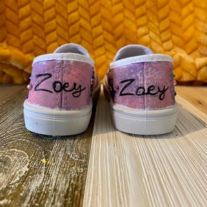 Puede incluir: Un par de zapatos de lona rosa y blanco con el nombre "Zoey" bordado en cada zapato.