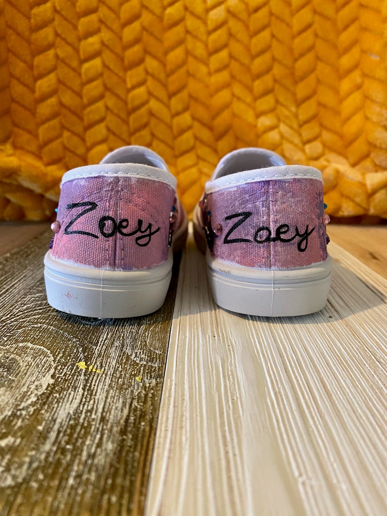 Puede incluir: Un par de zapatos de lona rosa y blanco con el nombre "Zoey" bordado en cada zapato.