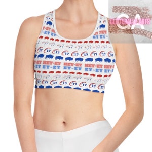 May include: White sports bra with a blue and red pattern featuring buffalo silhouettes and the text "HEY-EY" repeated. The bra has a racerback style.