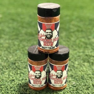 Puede incluir: Tres frascos de vidrio de condimento Baseball BBQ Diamond Dirt Rub. Los frascos están apilados uno encima del otro. La etiqueta en los frascos presenta una imagen de dibujos animados de un hombre barbudo y el texto "Baseball BBQ Diamond Dirt Rub".