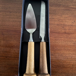 May include: A set of two silver cake knives with wooden handles. The handles are shaped like baseball bats.