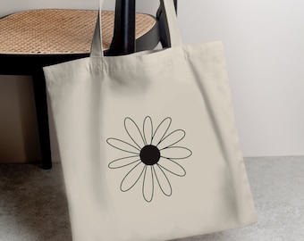 May include: A beige canvas tote bag with a black and white daisy design. The daisy has a black center and white petals.