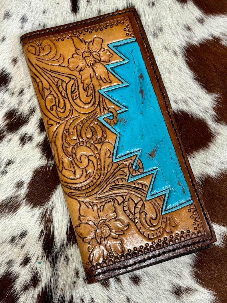 Peut inclure: Un portefeuille en cuir fait &agrave; la main avec des motifs floraux complexes et un motif en zigzag turquoise. Le portefeuille est de couleur marron clair avec des bordures marron fonc&eacute; et un motif floral en relief d&eacute;taill&eacute;.