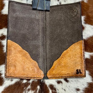 Peut inclure: Portefeuille en cuir marron ouvert avec des accents de design paisley tan en relief. Le portefeuille est maintenu ouvert avec une pince &agrave; reliure noire. Le fond est un motif de peau de vache.