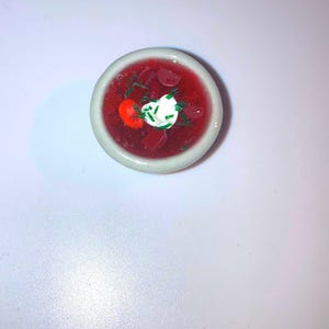 Peut inclure: Un petit bol blanc rempli de soupe rouge à la betterave, surmonté d'une cuillerée de crème fraîche et d'oignons verts hachés.