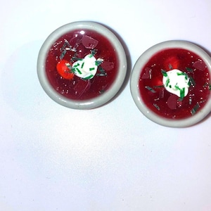 Peut inclure: Deux petits bols blancs remplis de soupe rouge au bortsch garnie de crème fraîche et d'oignons verts hachés.