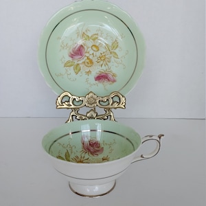 Peut inclure: Une tasse à thé et une soucoupe vintage avec un motif floral délicat. La tasse et la soucoupe sont toutes deux de couleur vert pâle avec une bordure dorée. Le motif floral présente des roses roses et jaunes et d'autres fleurs.