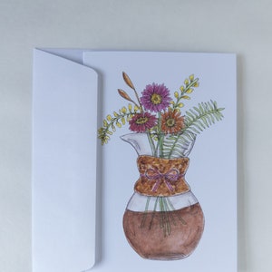 May include: A watercolor illustration of a glass carafe with a brown ribbon tied around the neck. The carafe is filled with a bouquet of pink, red, and yellow flowers.