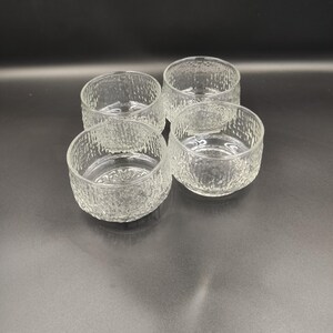 May include: Set of four clear glass bowls with a textured surface. The bowls are round and have a slightly flared lip.
