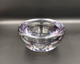 May include: A clear glass candle holder with purple and white swirls. The holder is round and has a wide opening at the top.