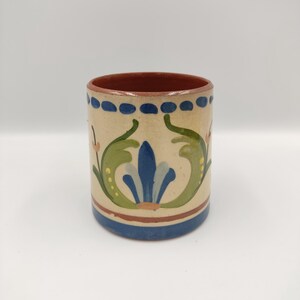 Może przedstawiać: Mały, ręcznie malowany kubek ceramiczny z niebieskim, zielonym i żółtym wzorem kwiatowym. Kubek ma brązową krawędź i białe tło.