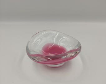 May include: A clear glass bowl with a pink interior. The bowl has a wavy, organic shape.