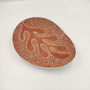 May include: A large, oval ceramic serving dish with a brown glaze and white polka dots. The dish features a white stylized leaf design.