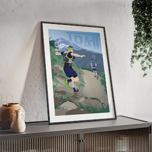 Peut inclure: Une affiche encadrée représentant deux coureurs sur un sentier de montagne. Le mot "TRAIL" est affiché en grandes lettres bleu clair au-dessus du paysage montagneux. Les coureurs sont représentés en mouvement.